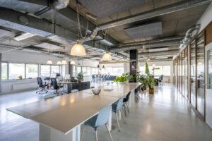 Moderne, open kantoorruimte aan de Anthony Fokkerweg met lange werktafels, bureaus, veel daglicht en groene planten.